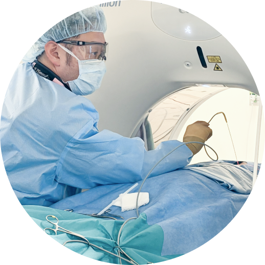 青い滅菌布で覆われた患者のそばで、医師が細い医療器具を用いて処置を行う様子